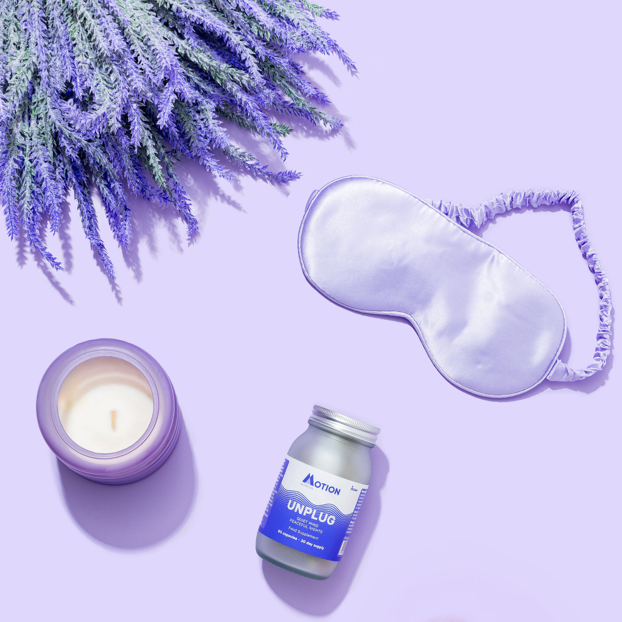 Sleep mask, candle, and 'UNPLUG' supplement bottle on a purple background with lavender.