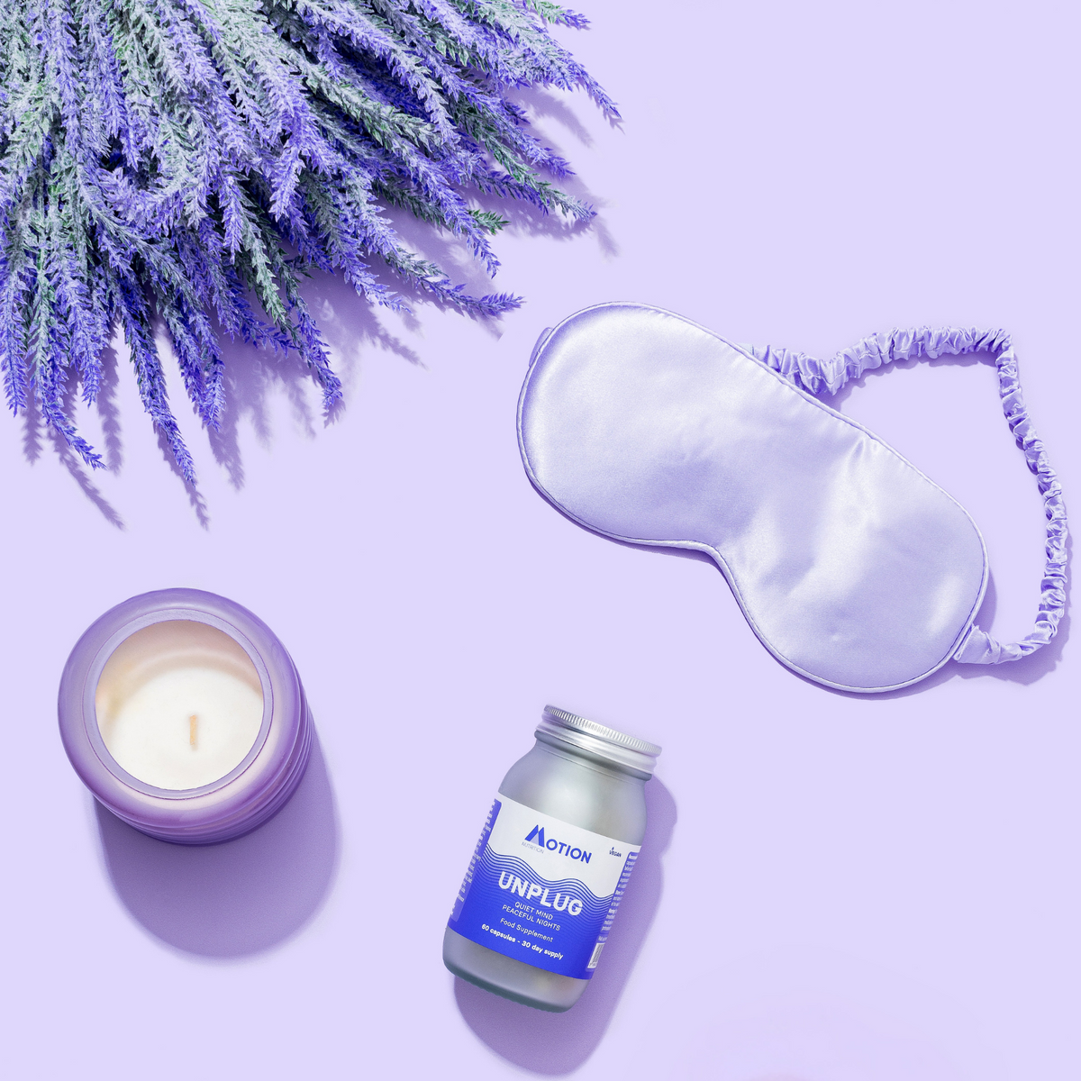Sleep mask, candle, and bottle labeled 'UNPLUG' on a purple background with lavender.
