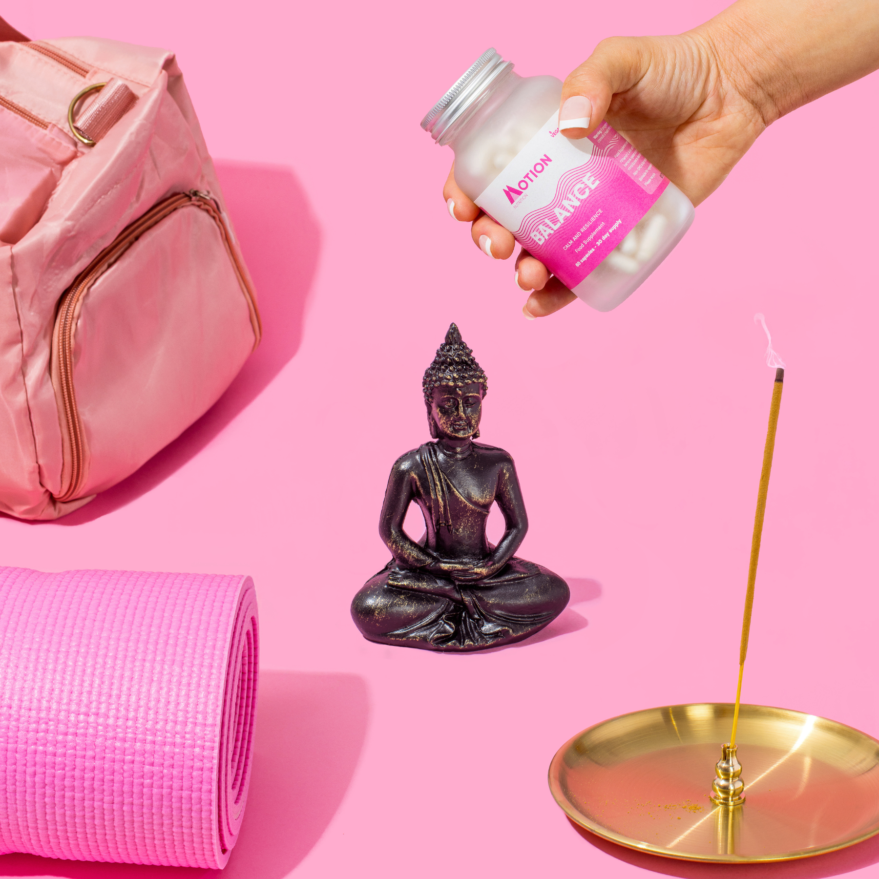 Pink bag, yoga mat, Buddha statue, and incense on a pink background with a hand holding a bottle labeled 'Balance'.