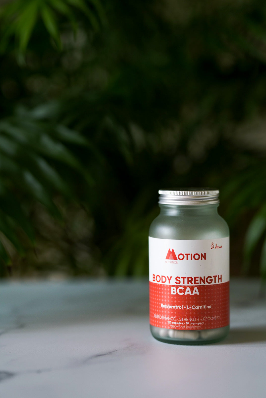 Bottle of Motion Body Strength BCAA on a surface with a blurred green background