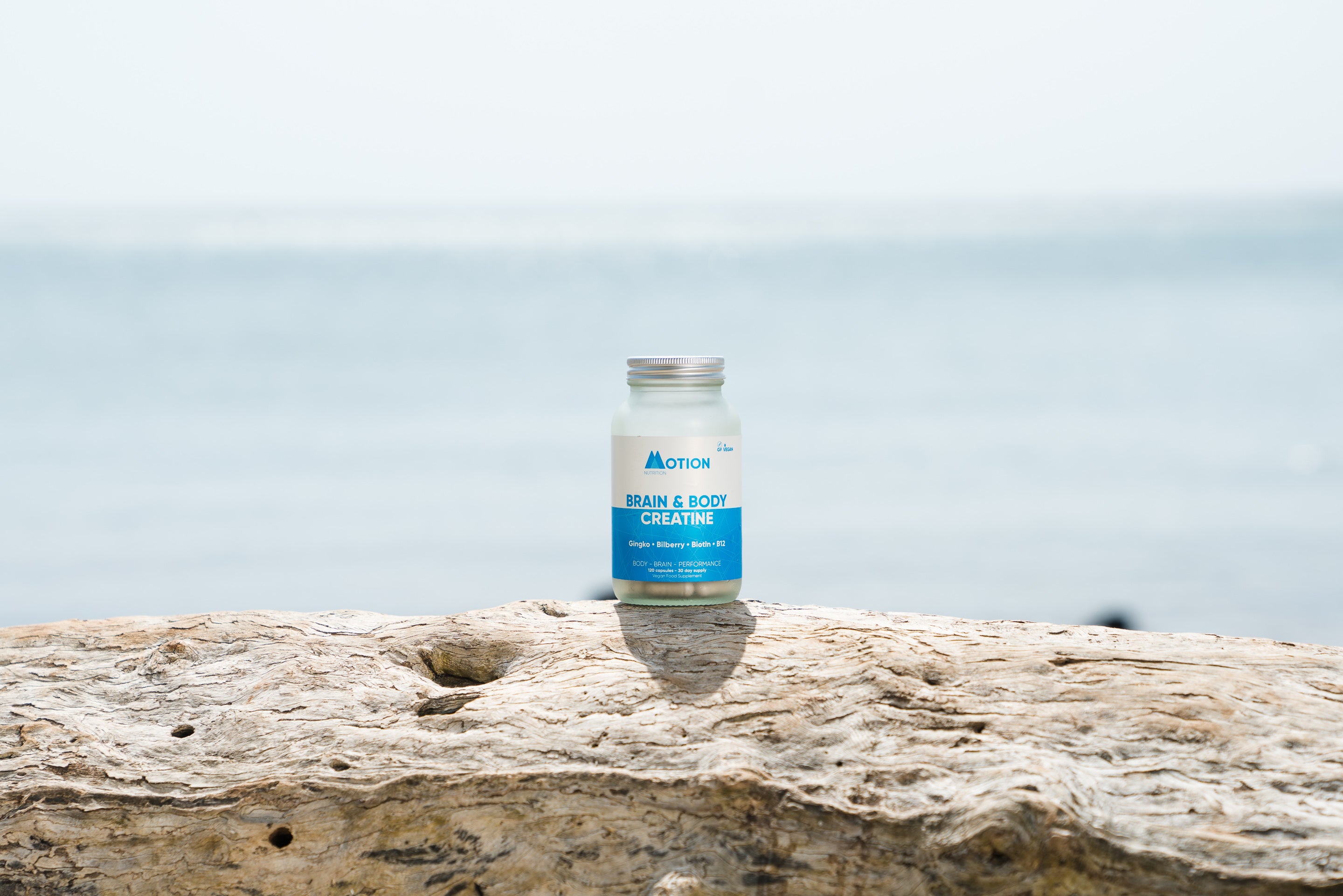 Bottle of motion creatine on a piece of driftwood with a blurred ocean background