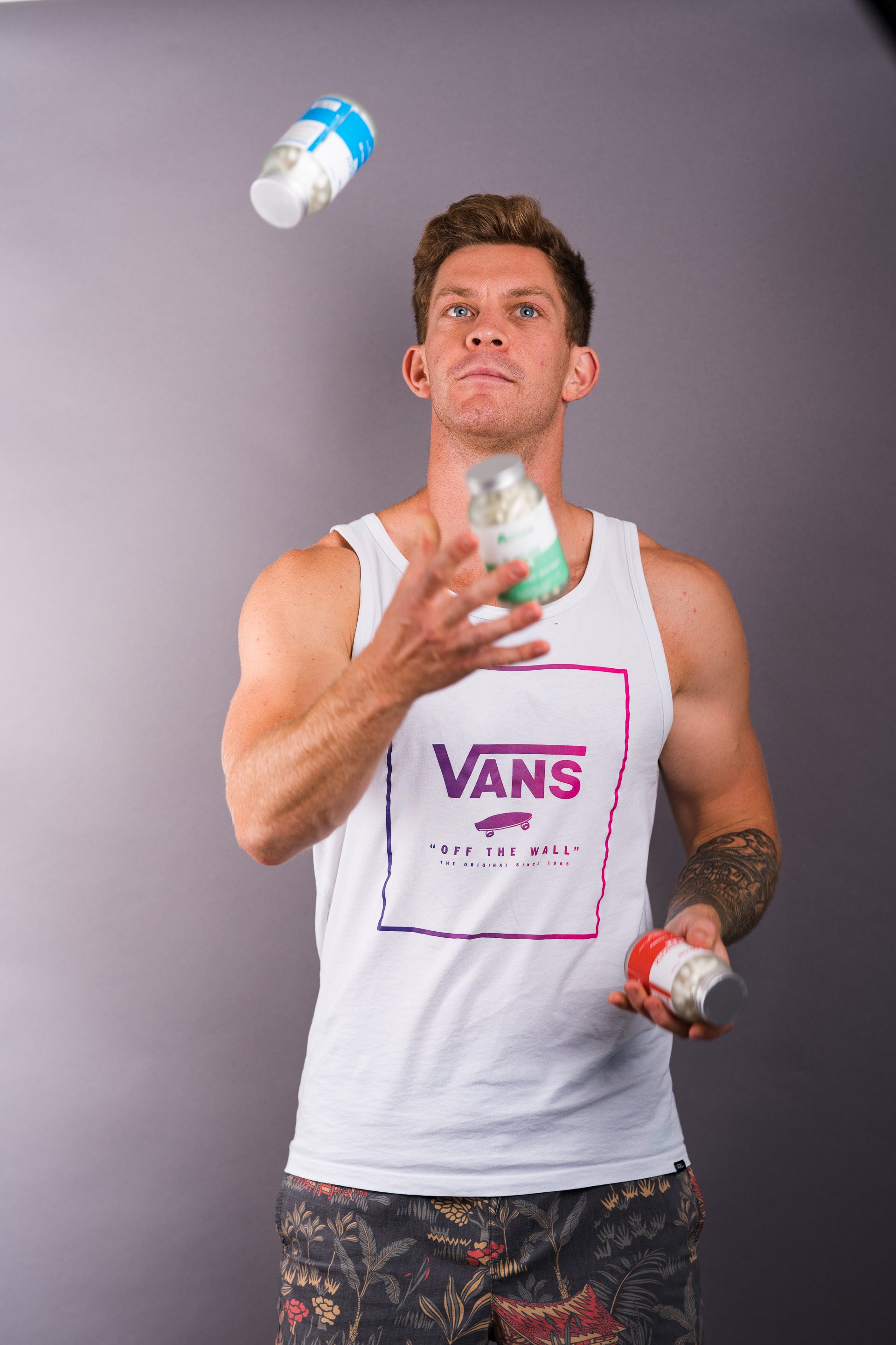 Man juggling spray bottles wearing a Vans tank top against a gray background